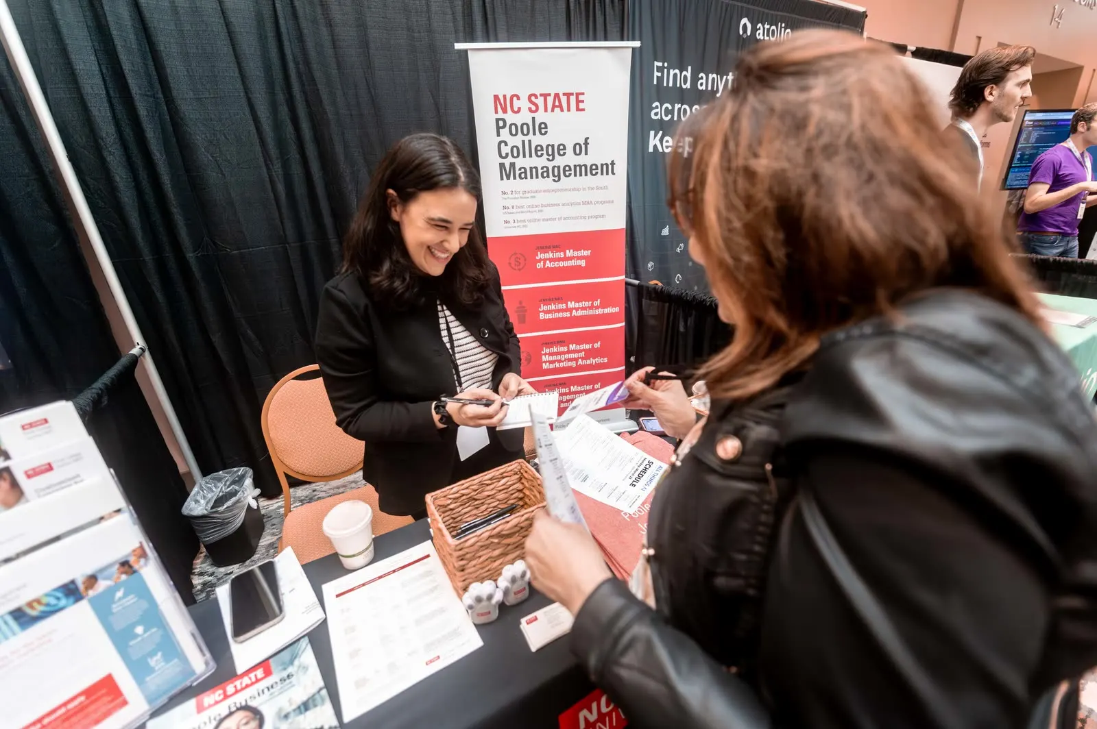Two people laughing together across the NC State Poole College of Management table at All Things AI 2026