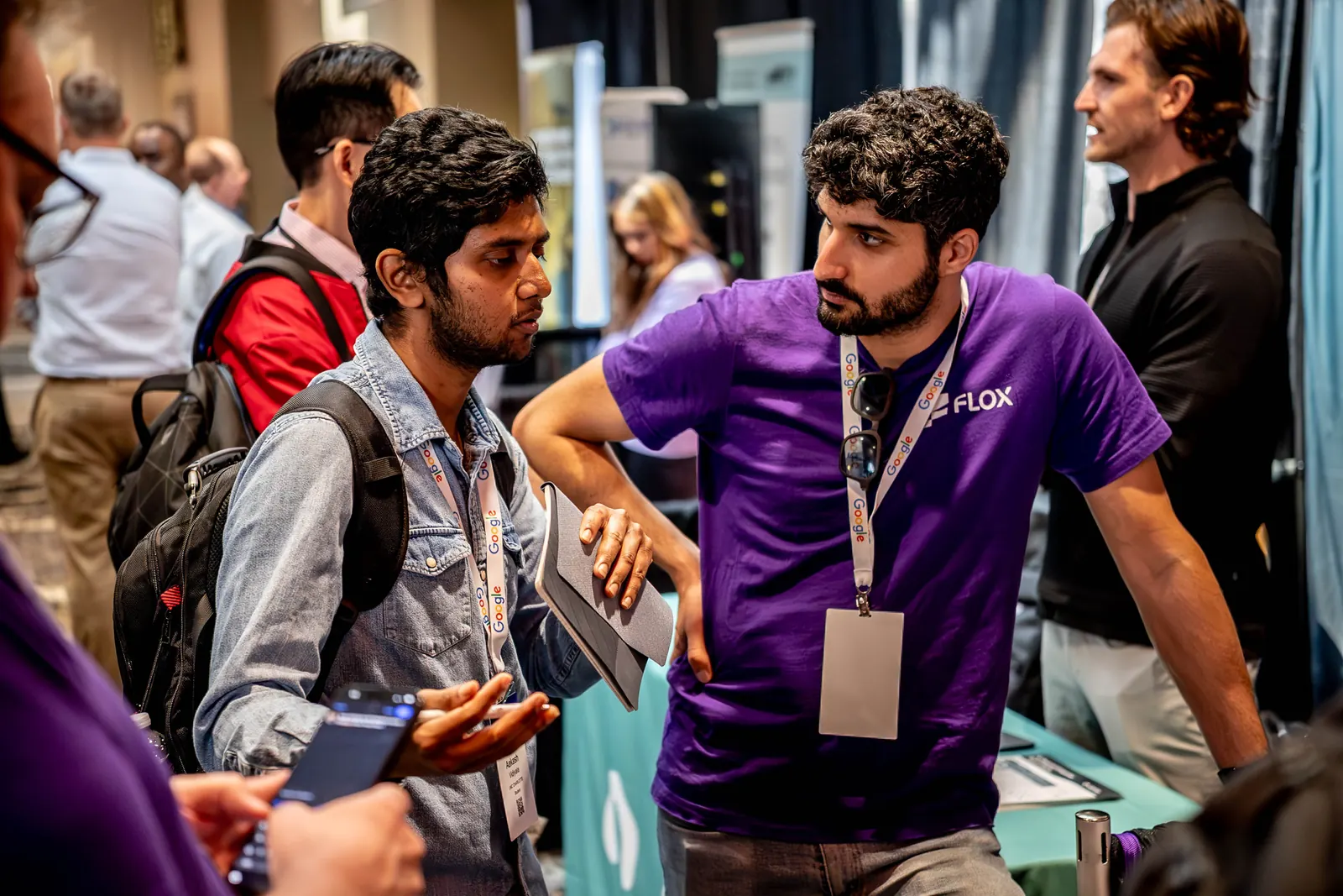 A Flox team member in a purple Flox shirt talking with attendees at the Flox table at All Things AI 2026