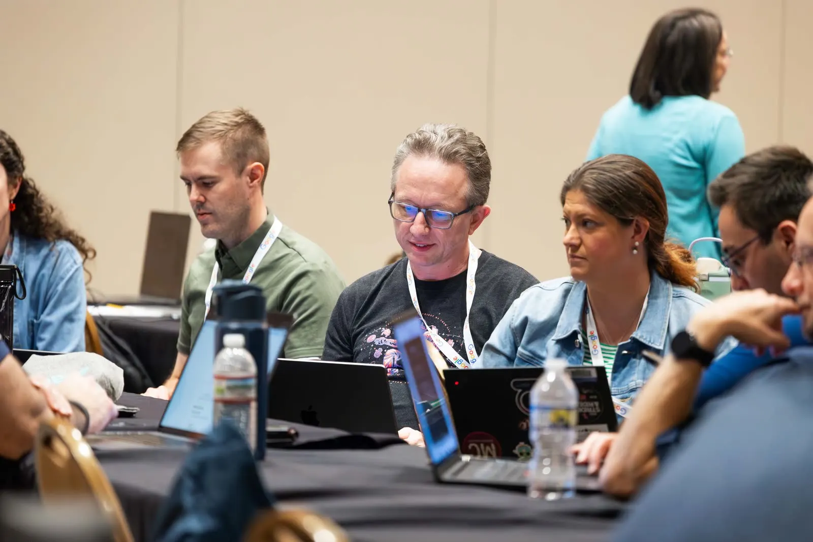 Three people side by side at a workshop table at All Things AI 2026, laptops open, working through an exercise