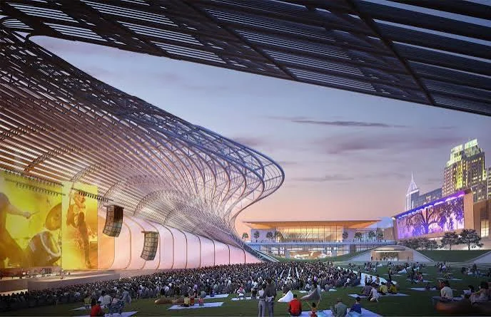 Architectural rendering of downtown Raleigh's convention district at dusk: an outdoor stage under a curved canopy, a crowd on the lawn, and the convention center and skyline behind