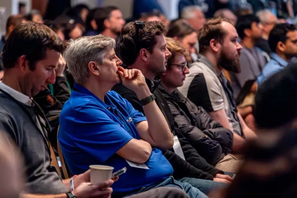 A row of attendees watching a session, including a listener with a notebook, at All Things AI 2026