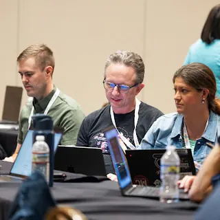 Workshop participants comparing notes around a table at All Things AI